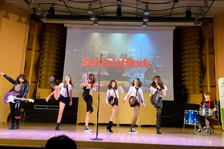 Elevii academiei pe scenă, cu microfoane și baterie, în spectacolul „School of Rock”
