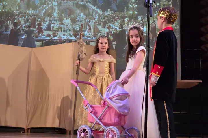 Doi copii în costume de epocă, cu un cărucior de păpuși, într-o scenă de spectacol
