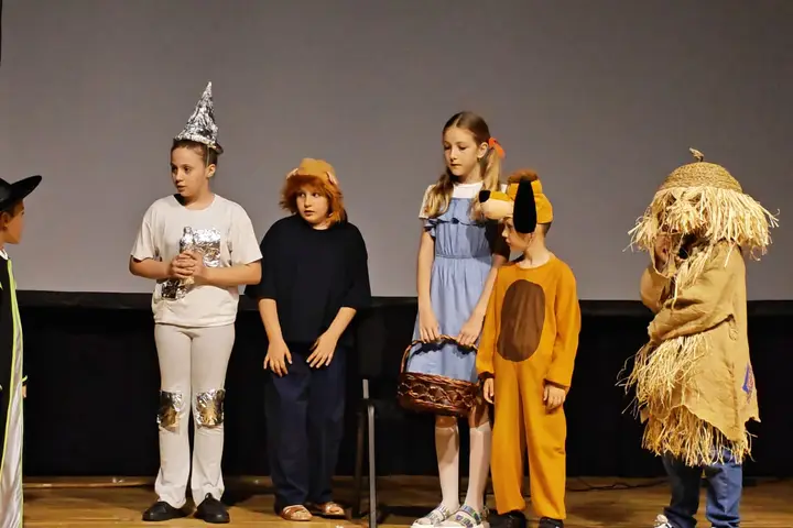 Distribuție în costume inspirate din „Vrăjitorul din Oz”, aliniată pe scenă