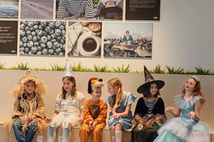 Copii în costume — sperietoare, leu, vrăjitoare și zână — așezați pe marginea scenei