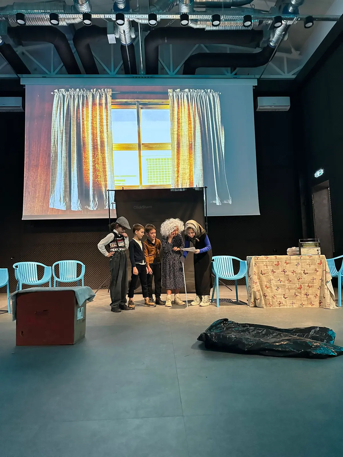 Scenă cu decor de fereastră proiectat și grupul de actori în plan îndepărtat